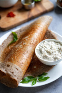 Thin, crispy reddish ragi dosa served with white coconut chutney and sambar